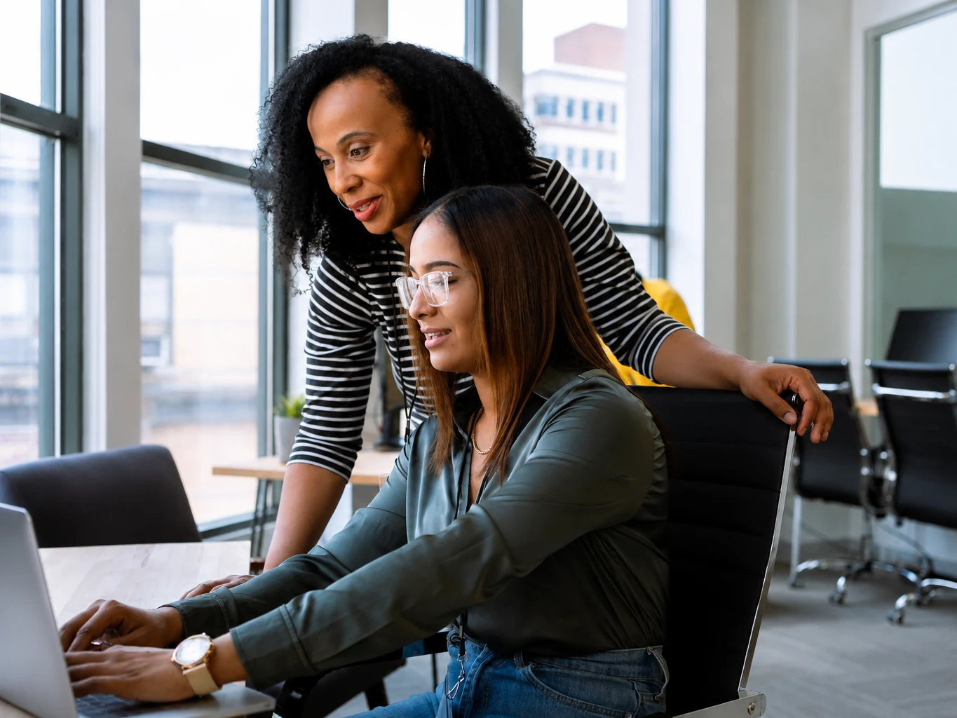 A postgraduate student working at a laptop while a mentor looks on